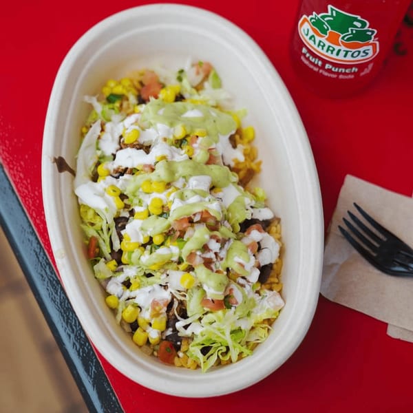 A Tacos and Tortilla Factory burrito bowl with corn, lettuce, and sauces, next to a Jarritos soda.