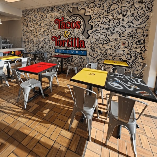 Interior of Tacos & Tortilla Factory with colorful tables, metal chairs, and a vibrant mural.