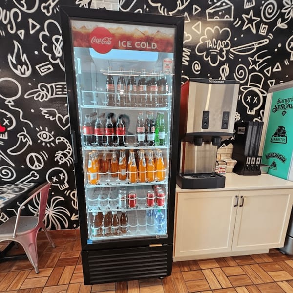 A Coca-Cola branded cooler filled with bottled and canned drinks next to an ice machine.