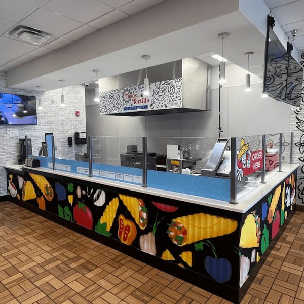 Tacos and Tortilla Factory's brightly lit counter with a colorful mural of Mexican food items.