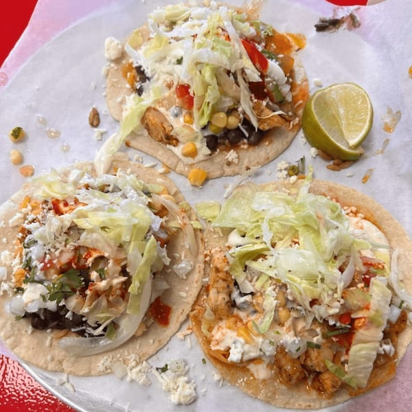 Three Tacos and Tortilla Factory tacos with chicken, lettuce, cheese, and a lime wedge.