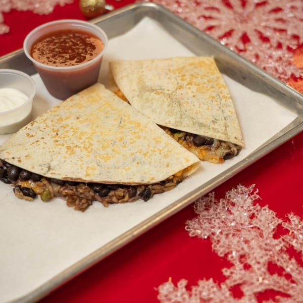 Two quesadilla halves filled with black beans and rice, served with salsa and sour cream.
