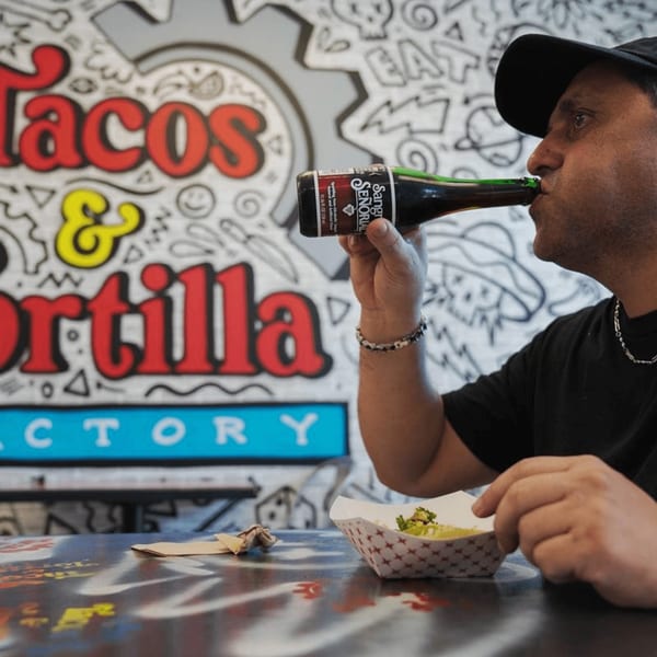Man in a black cap drinking from a Sangria Señorial bottle at Tacos and Tortilla Factory.