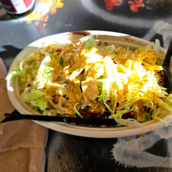 A Tacos and Tortilla Factory burrito bowl, topped with lettuce, cheese, and sauce.