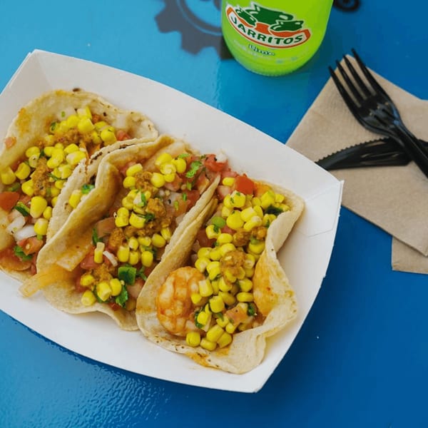 Three vibrant tacos with corn, salsa, and shrimp or ground meat, alongside a Jarritos soda.