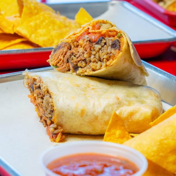 Two large burritos, one cut in half, revealing rice, beans, and meat, with tortilla chips and salsa.