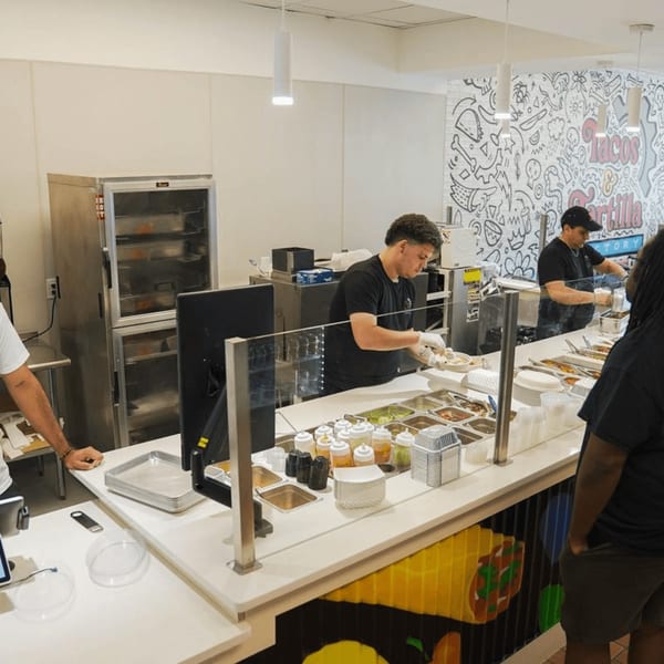 Staff preparing food behind a counter with various toppings at Tacos and Tortilla Factory.