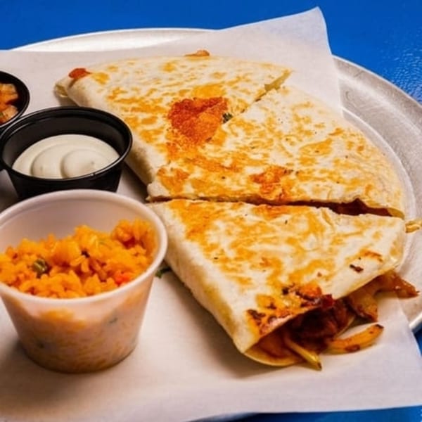 Two quesadilla halves with rice and sour cream on a metal plate, from Tacos and Tortilla Factory.